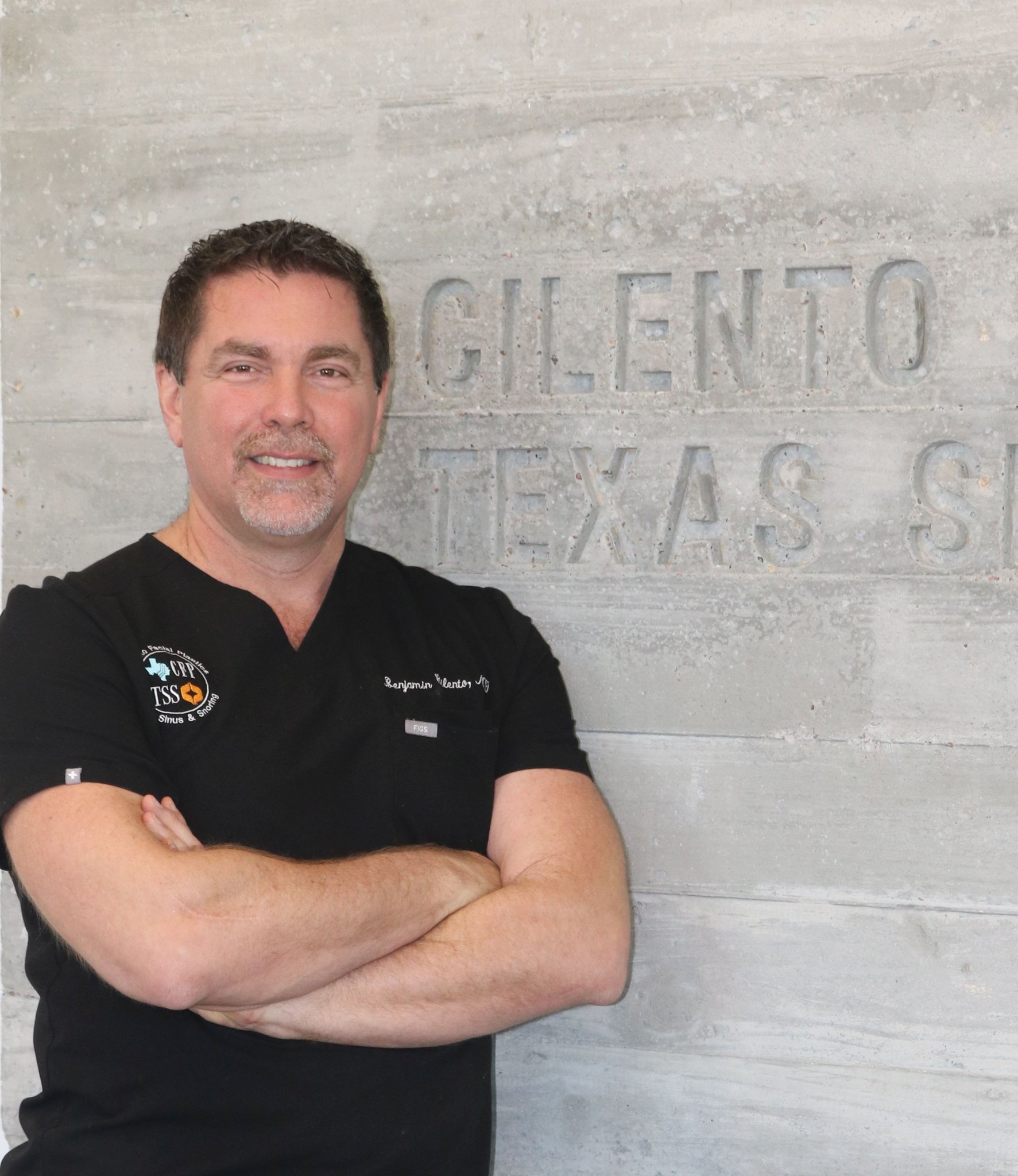 Dr. Ben Cilento, ENT surgeon, posing with arms crossed in front of Texas Sinus and Snoring signage
